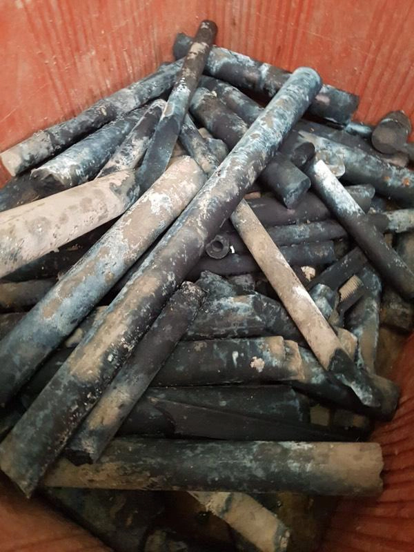 Barres de molybdène oxydées et noircies empilées dans un bac rouge, rebut de métal réfractaire