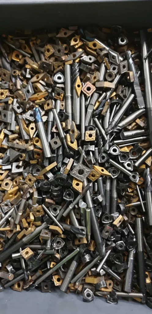 Tas de plaquettes carbure d’usinage CNC usagées en vrac, mélange de formes carrées, triangulaires et rondes avec forets et outils coupants